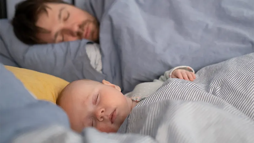 Un'immagine di un bambino che dorme accanto al papà.