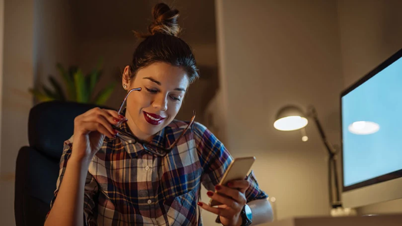 l'immagine di una donna che tiene in mano il suo telefono davanti a un computer