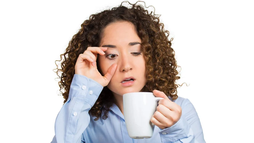 l'immagine di una donna che si sveglia intontita e beve una tazza di caffè