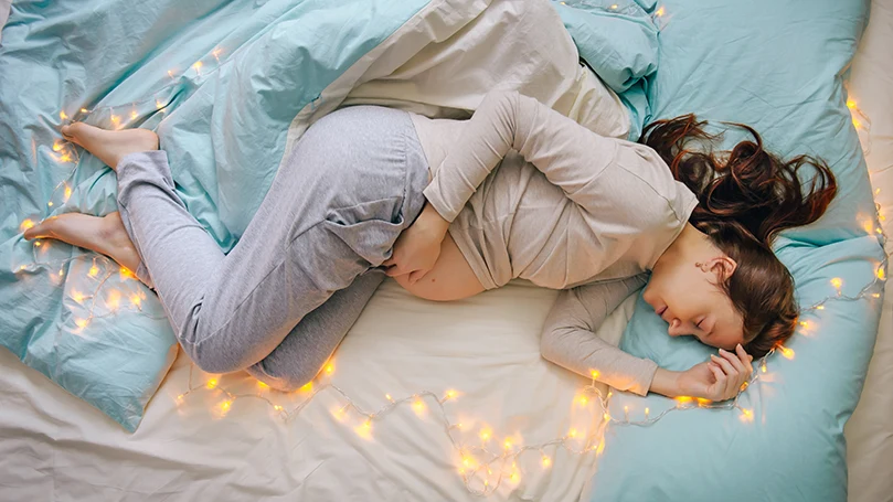 l'immagine di una donna incinta che dorme in un letto con la luce accesa