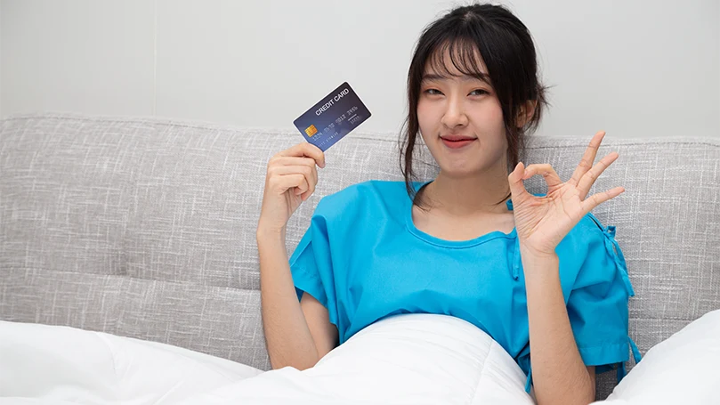 Una donna asiatica a letto con la carta di credito in mano