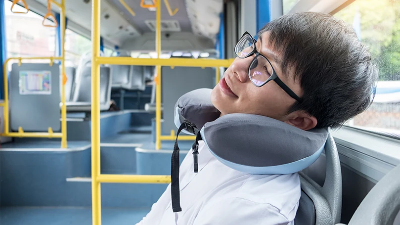 Un uomo dorme con un cuscino cervicale in autobus