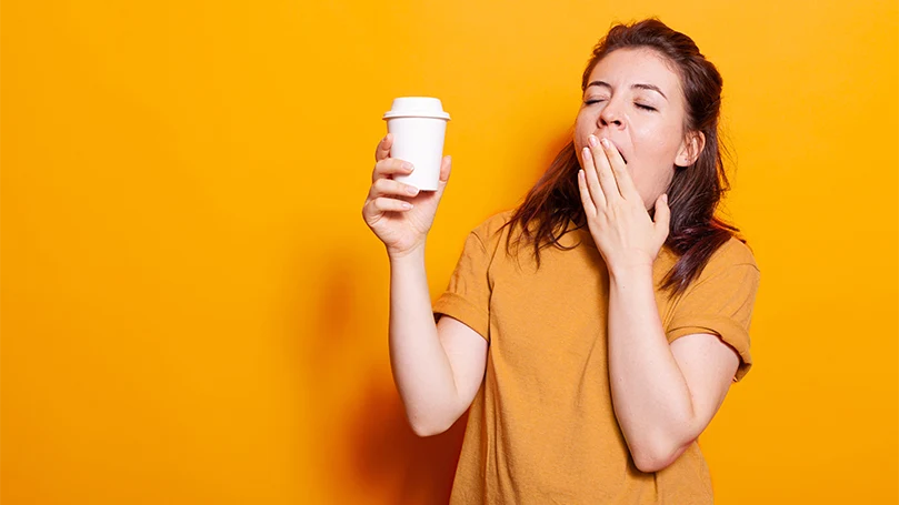 Una donna assonnata con in mano una tazza di caffè.