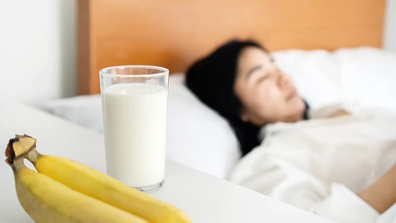 L'immagine di una donna che dorme accanto a un comodino con latte e banane.