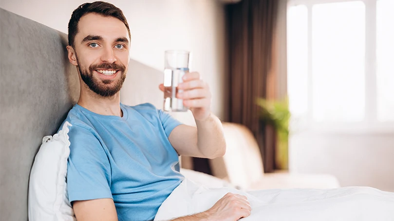 Immagine di un uomo che beve un bicchiere d'acqua nel suo letto prima di andare a dormire.