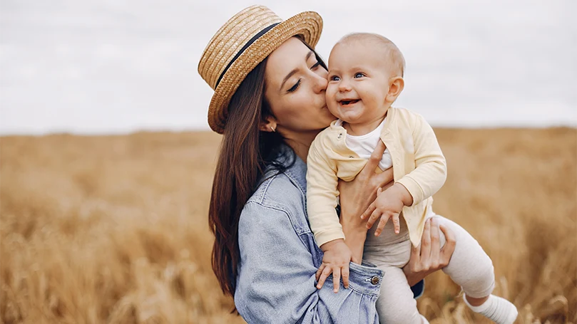 Un'immagine di una mamma che tiene in braccio il suo bambino nel campo.