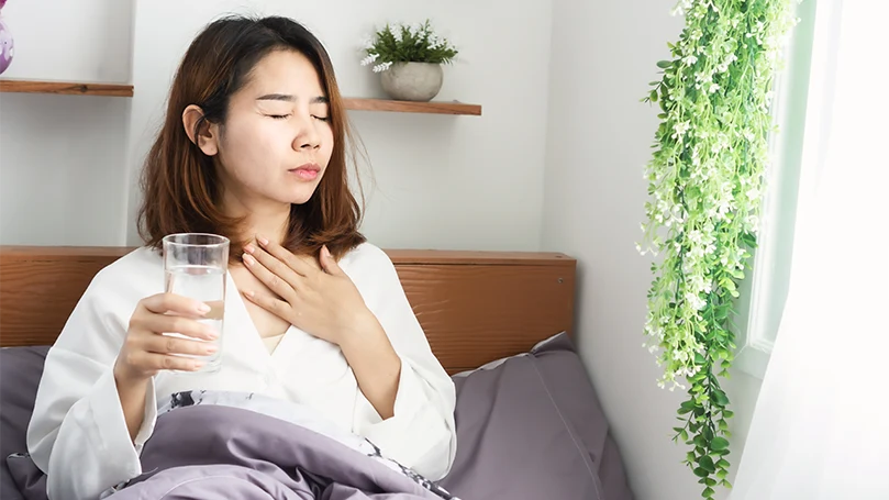 Immagine di una donna asiatica giovane e malata che beve acqua a letto prima di dormire.