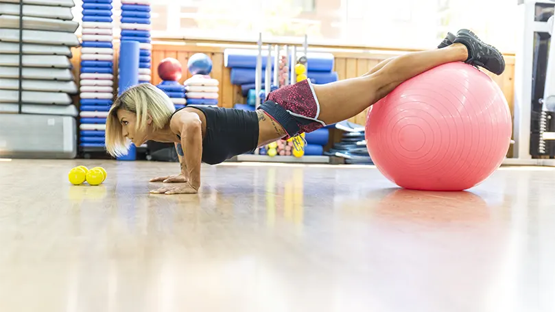 Un'immagine di una donna che esegue flessioni in declinazione su una palla da yoga