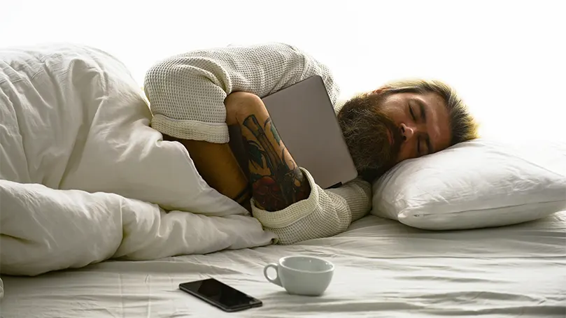 Un'immagine di un uomo barbuto nel sonno profondo che abbraccia una tavoletta.