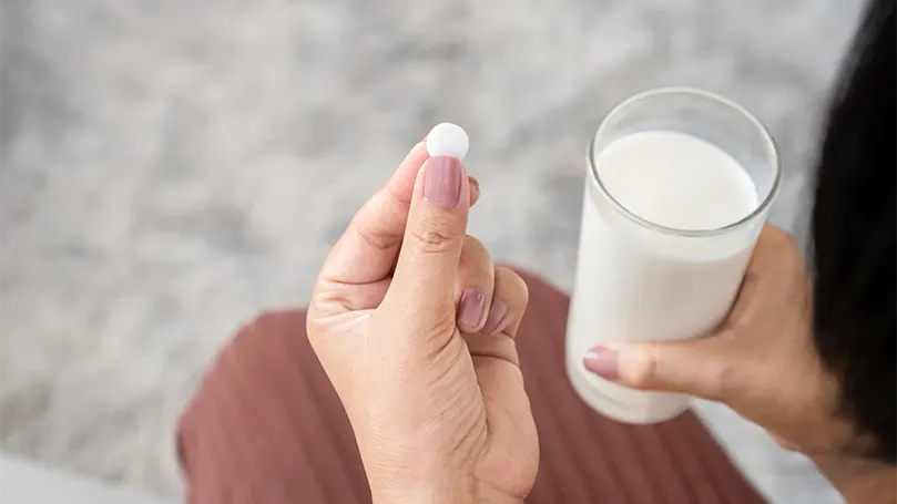 Una donna che assume una pillola di melatonina con un bicchiere di latte.