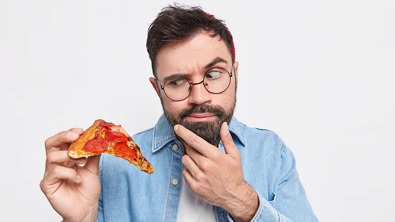 un uomo barbuto che tiene in mano una fetta di pizza