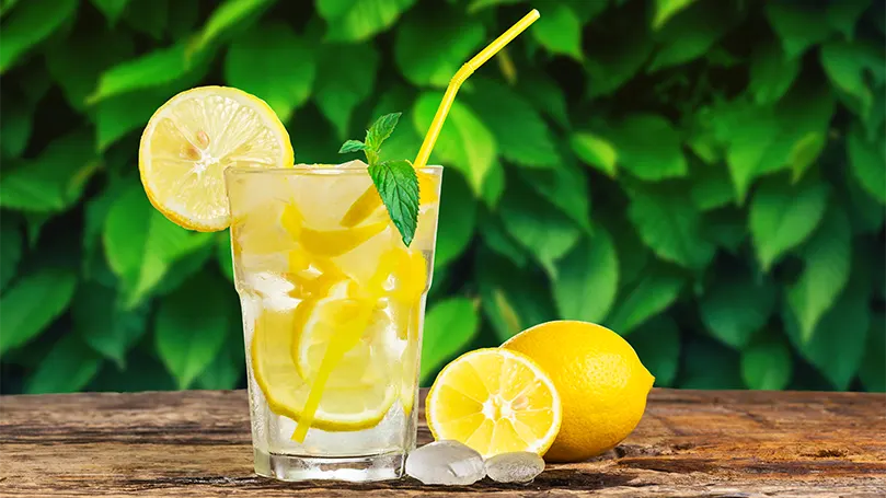 un bicchiere di acqua e limone accanto a due limoni su un tavolo.