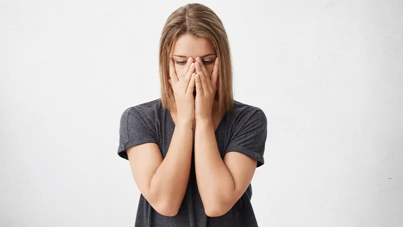 Immagine di una donna con le mani che si coprono il viso mentre soffre di sintomi di stanchezza invernale