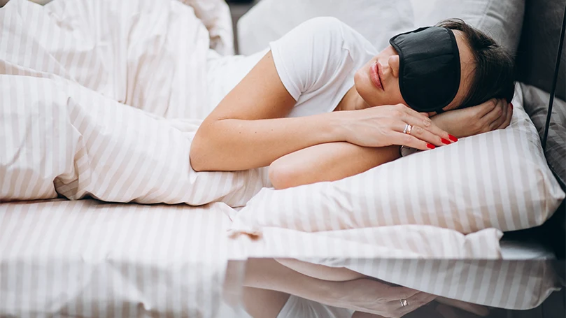 Un'immagine di una donna con una maschera per dormire che dorme nel letto