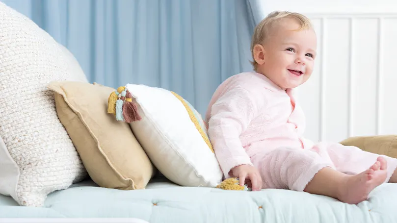 An image of a child sitting on a bed next to a few toddler pillows